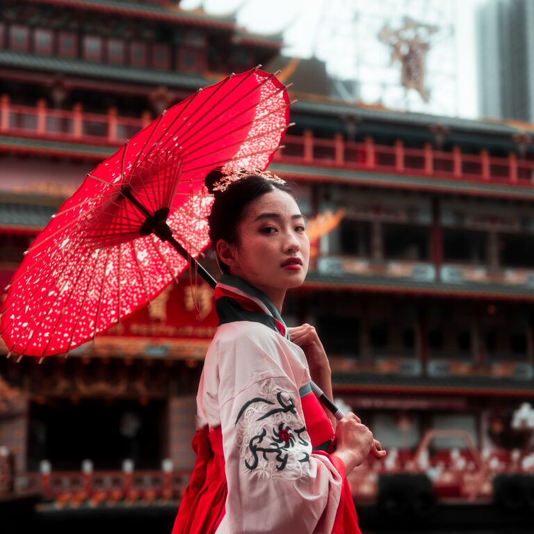 Eine rot-weiß gekleidete Japanerin mit einem rotem Sonnenschirm